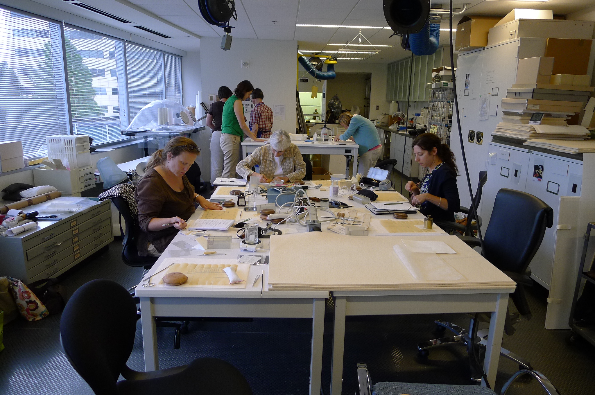FAIC Conservation of Transparent Papers workshop, July 17-18 and July 19-20, 2012 at SIA. Taught by Hildegard Homburger. Photo by Nora Lockshin. People sit and stand at workstations and work on documents.