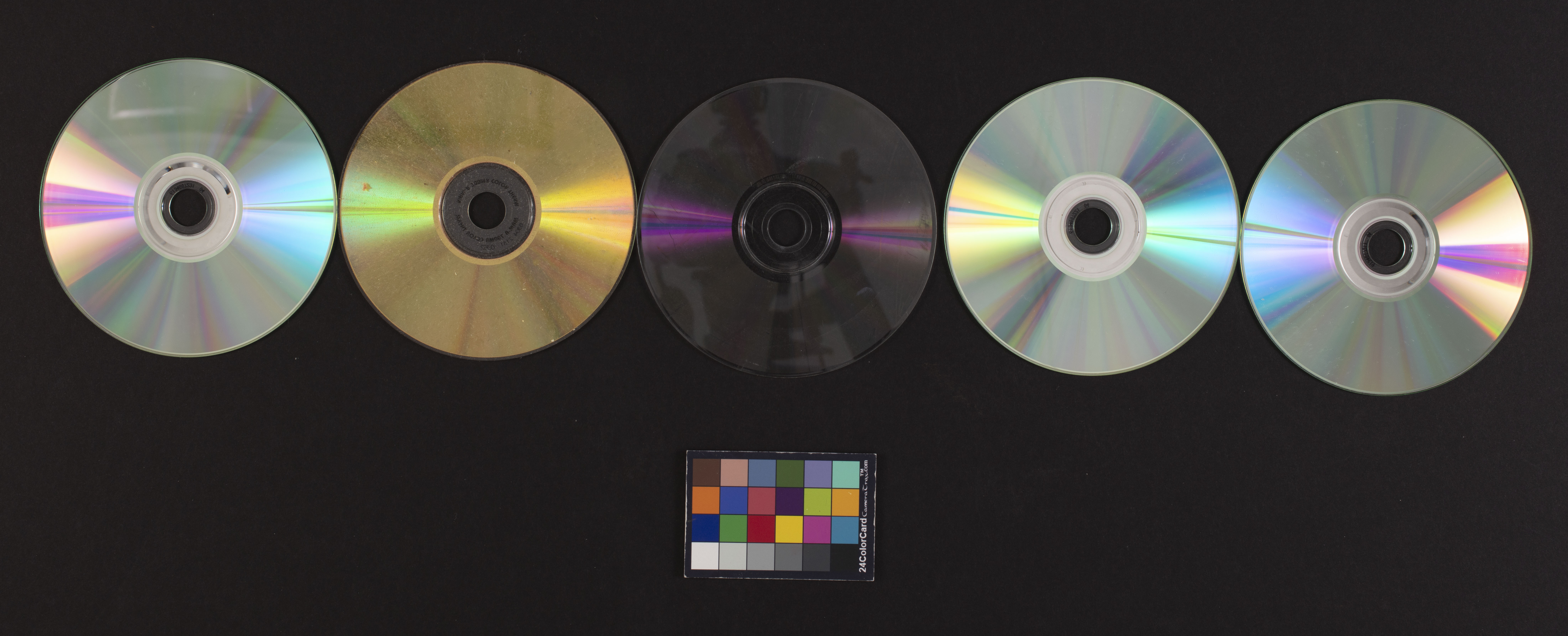Figure 1. One of our first photography tests involved multiple CDs. We decided that photographing one disc at a time was better to get more even lighting across the surface and to reduce lens flare. October 18, 2019. Courtesy of Miguel Resendiz. Five CDs and a color card against a black background.