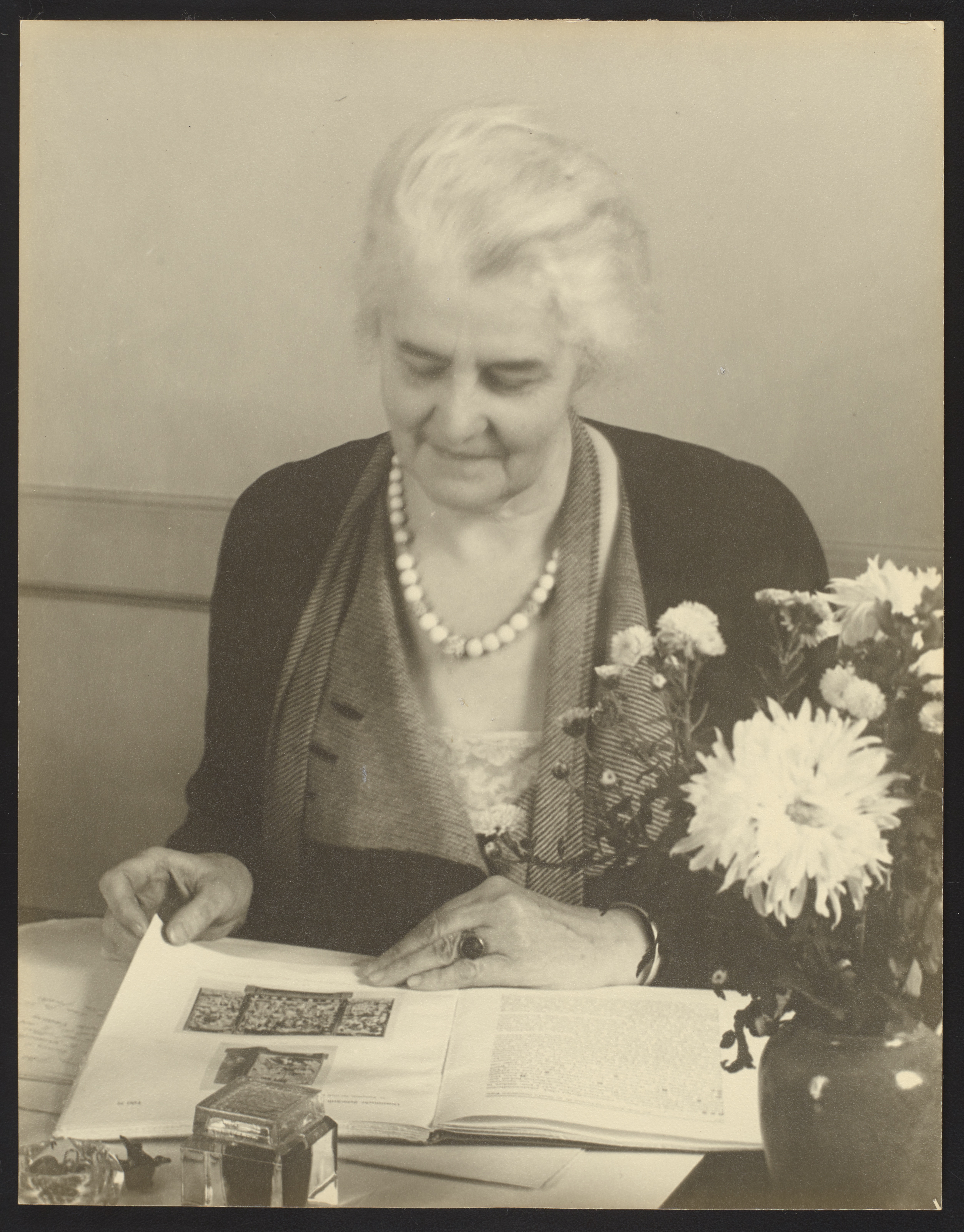 Grace Dunham Guest, c. 1940, photographer unknown, Smithsonian Institution Archives, Accession 02-007, Box 1, Image no. SIA2021-003662. Portrait photograph of Guest seated at a desk. She has a book open and is looking down at it.
