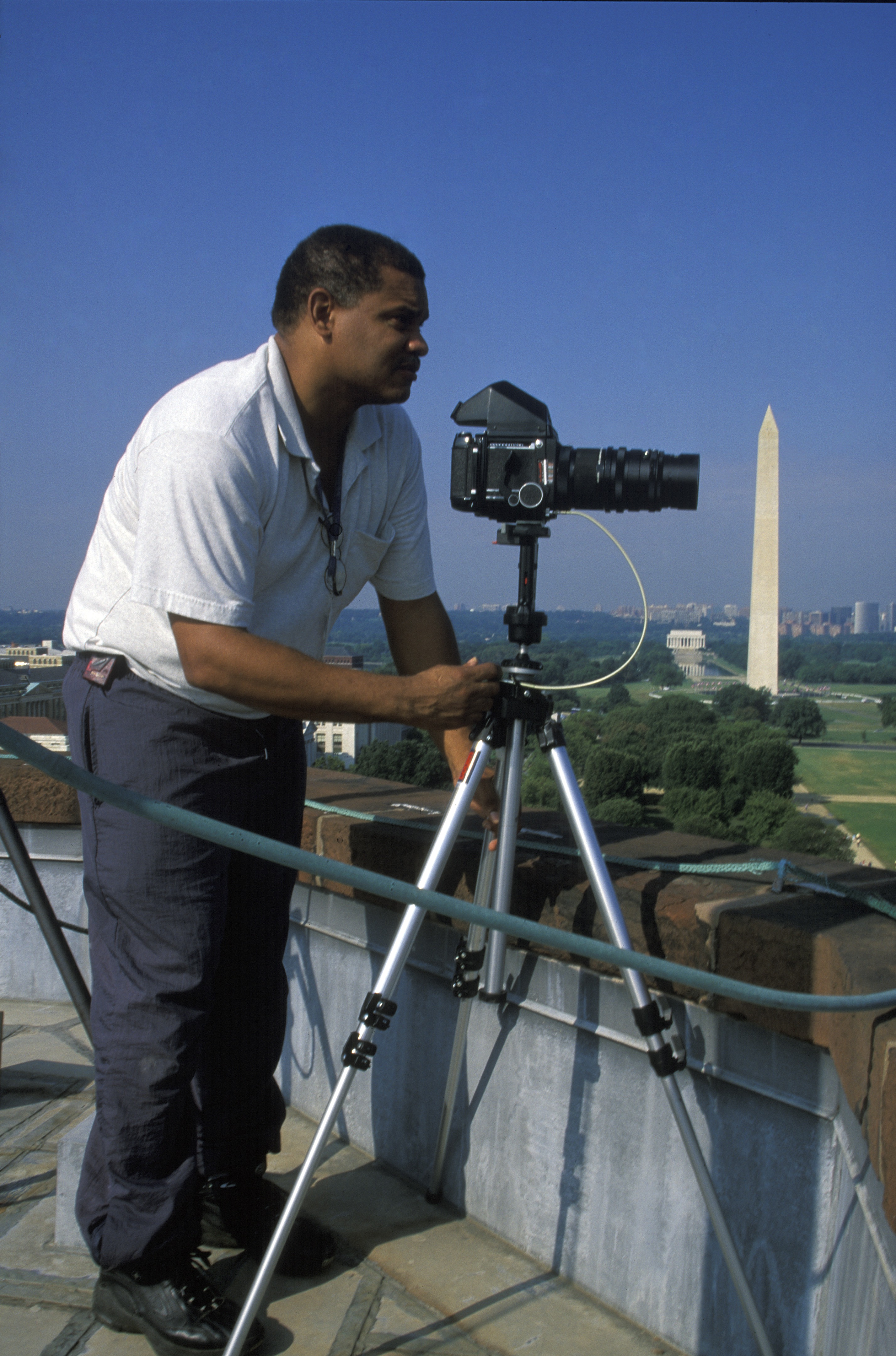 Michael Barnes stands on a rooftop and leans to a camera on a tripod.