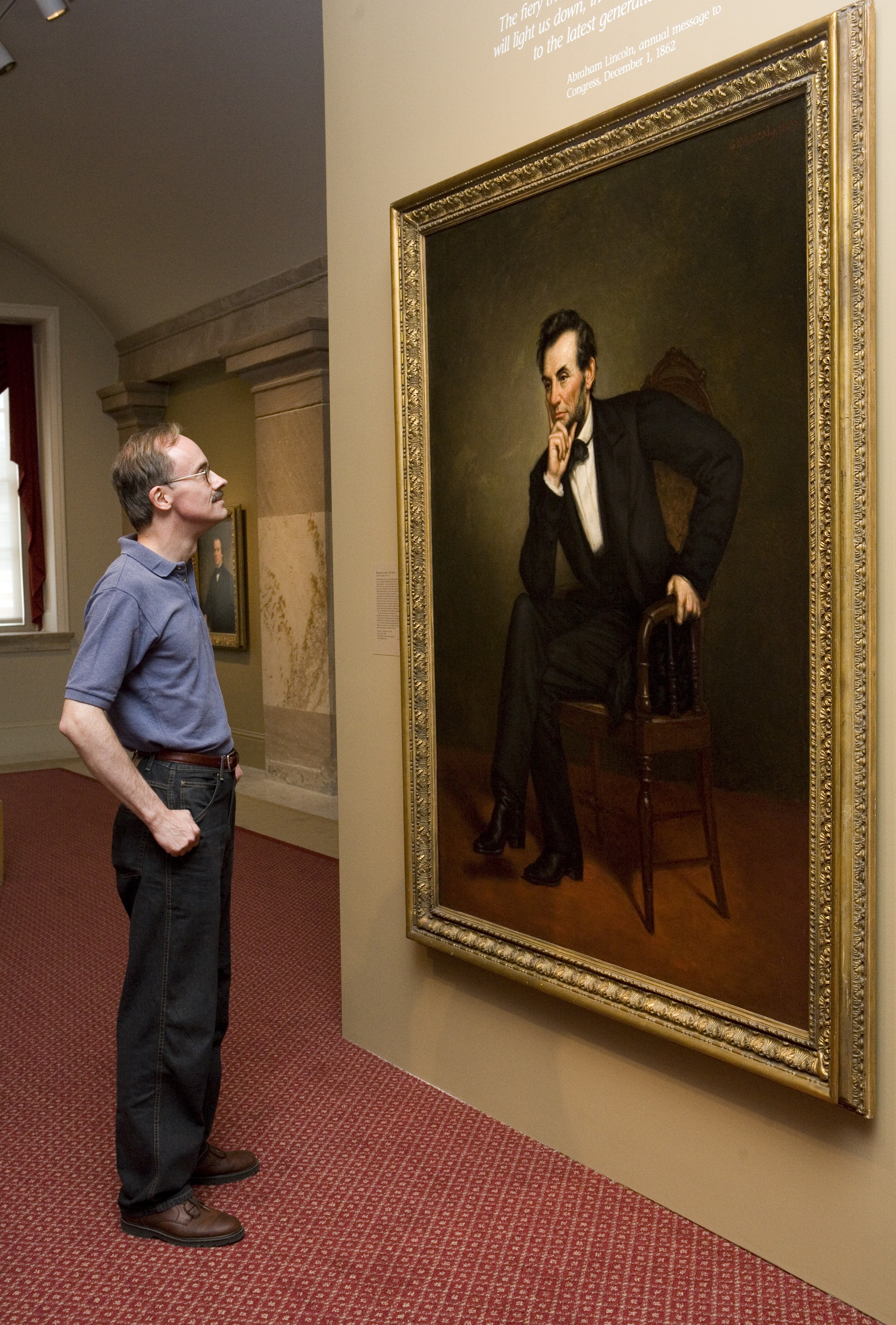 A man stands in front of a large portrait of Abraham Lincoln.