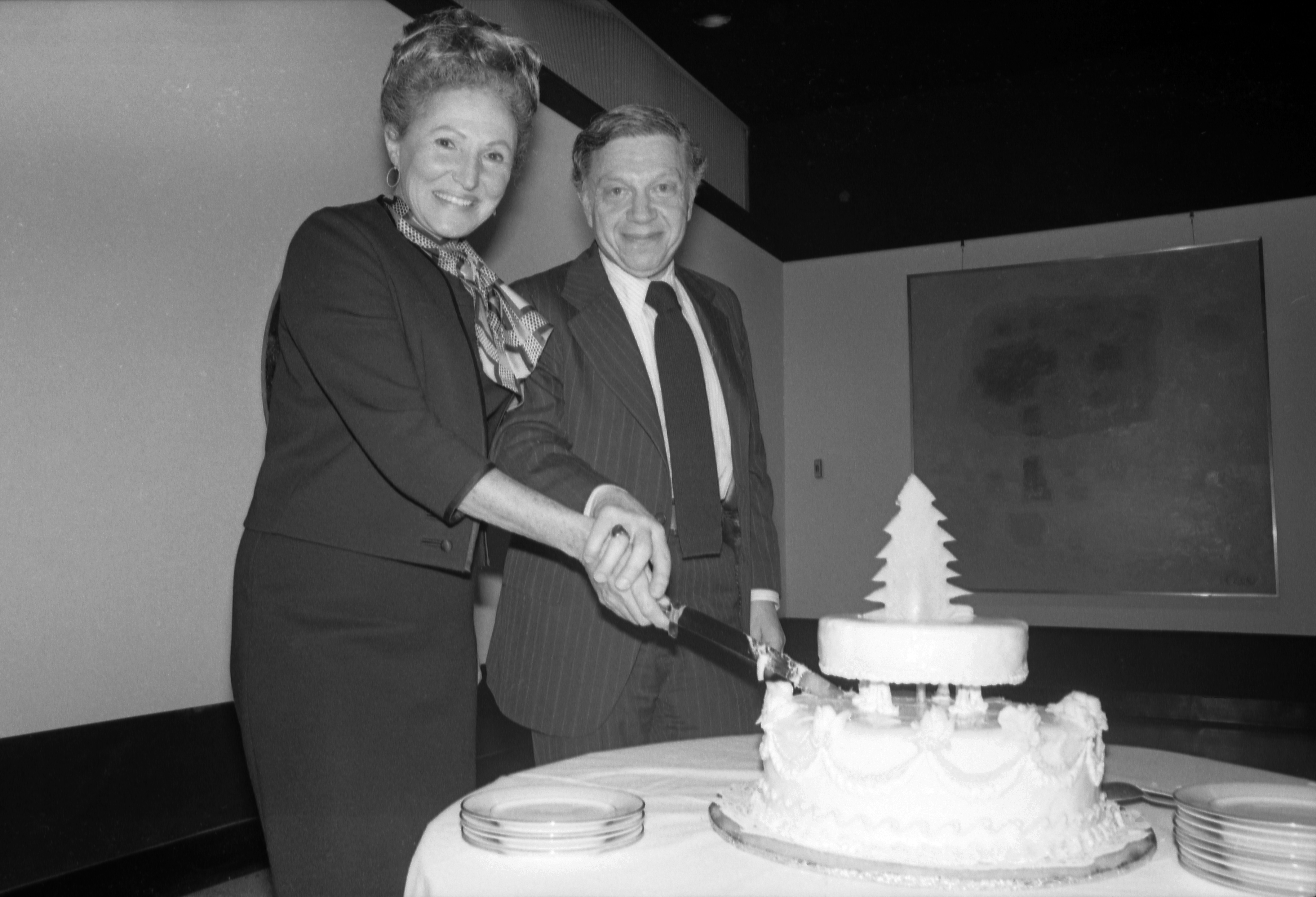 Two persons standing and smiling while cutting a cake.