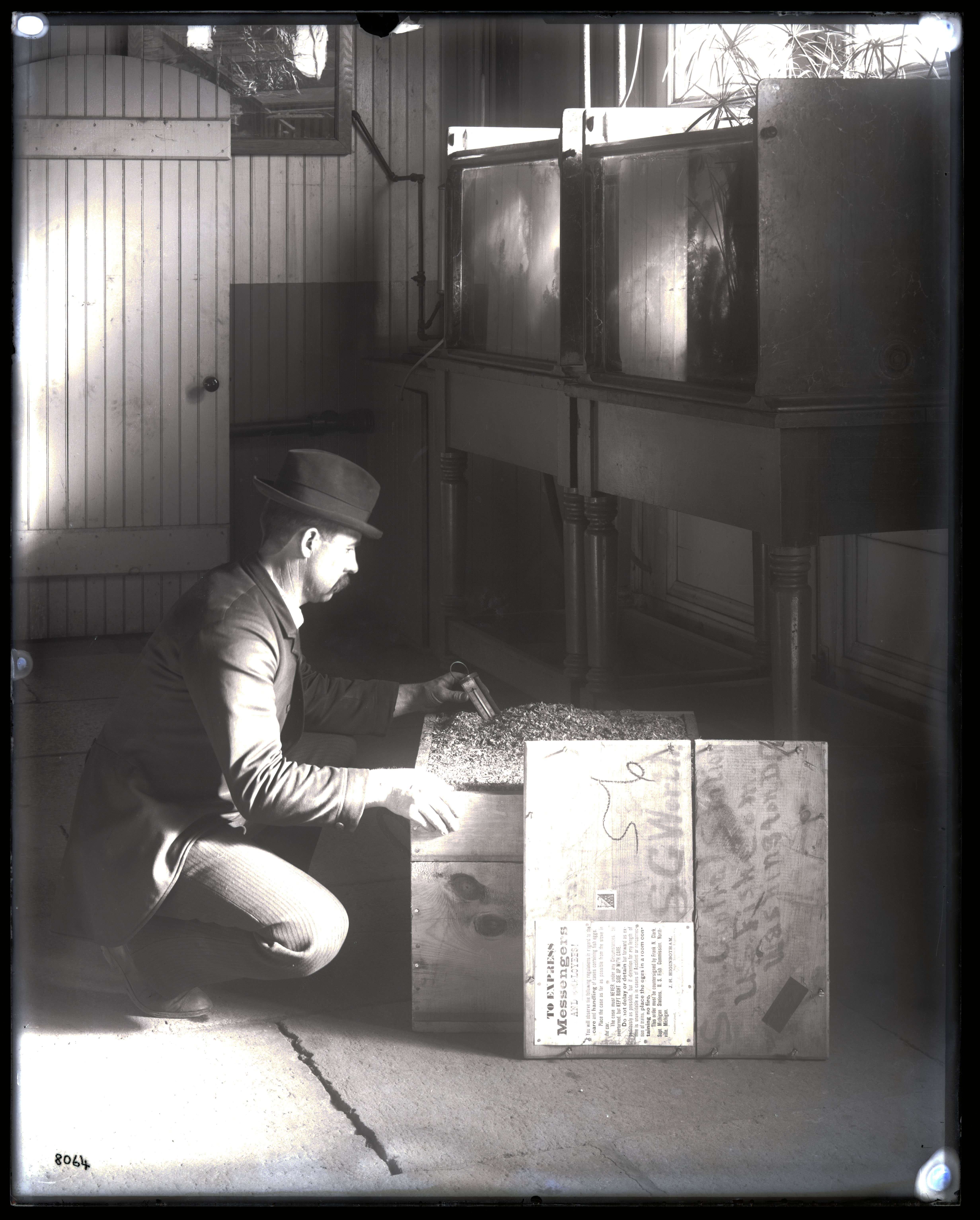 Black and white image of man kneeling beside wooden crate.