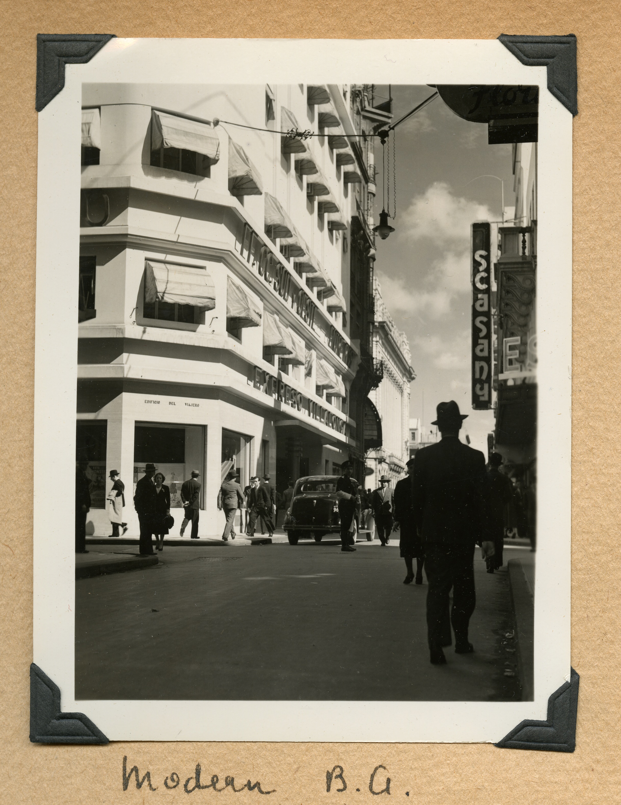 Image in a scrapbook of a busy street with people walking on sidewalks and on the street. The people
