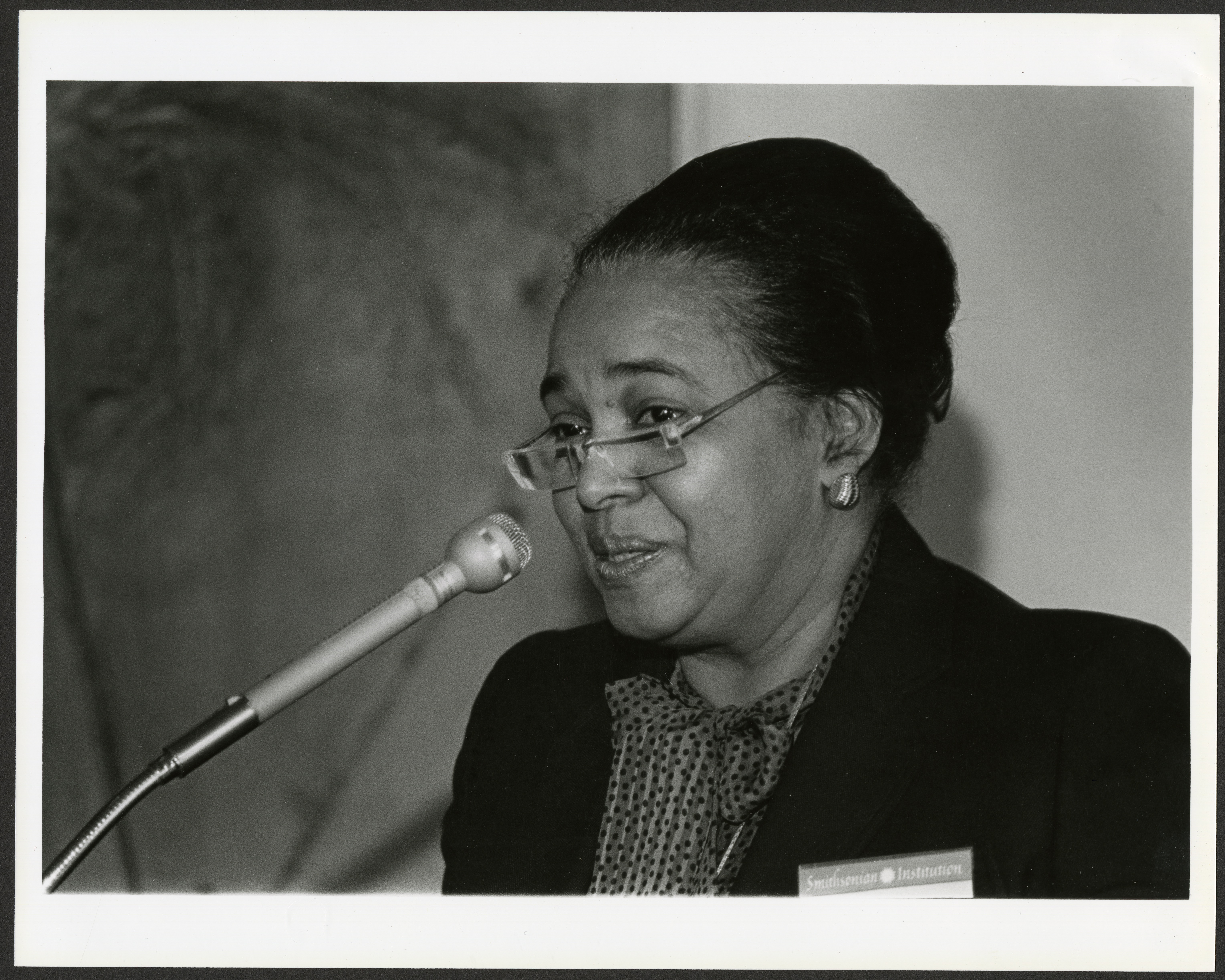 Black and white photograph of woman speaking at microphone.
