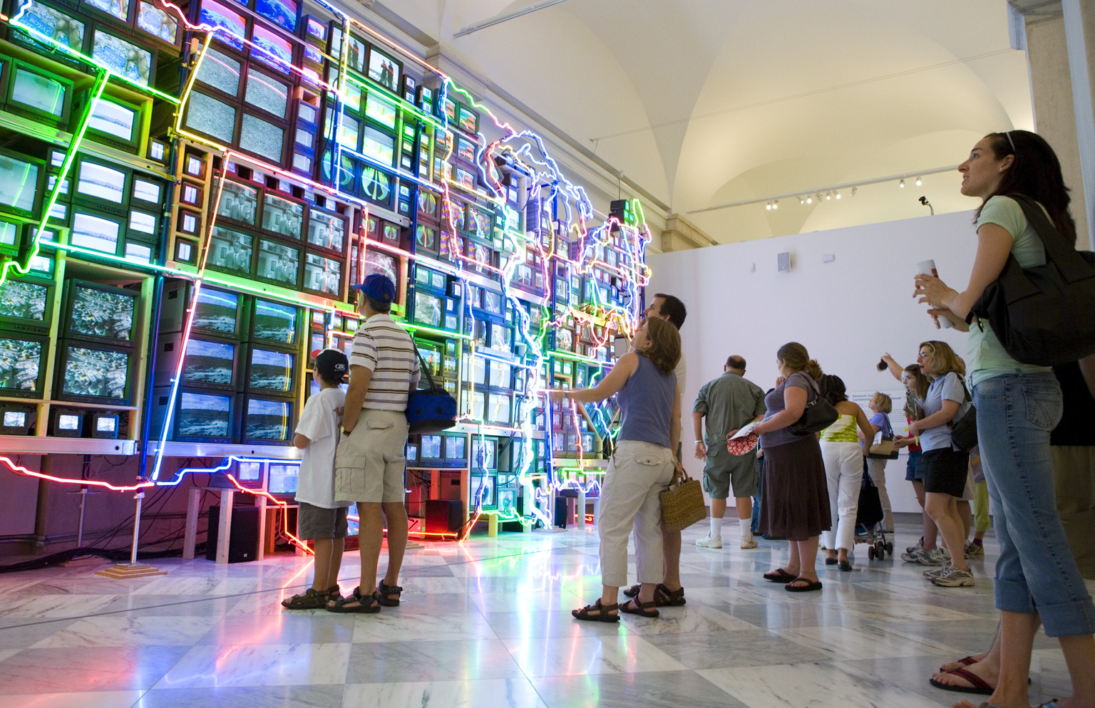 People look at a map of United States of a fifty-one channel video installation with neon outlines.