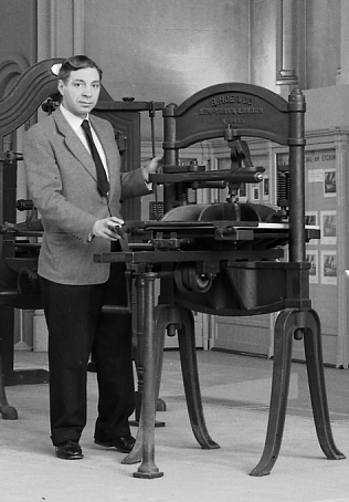 Black and white photograph of man in suit next to unknown metal object.