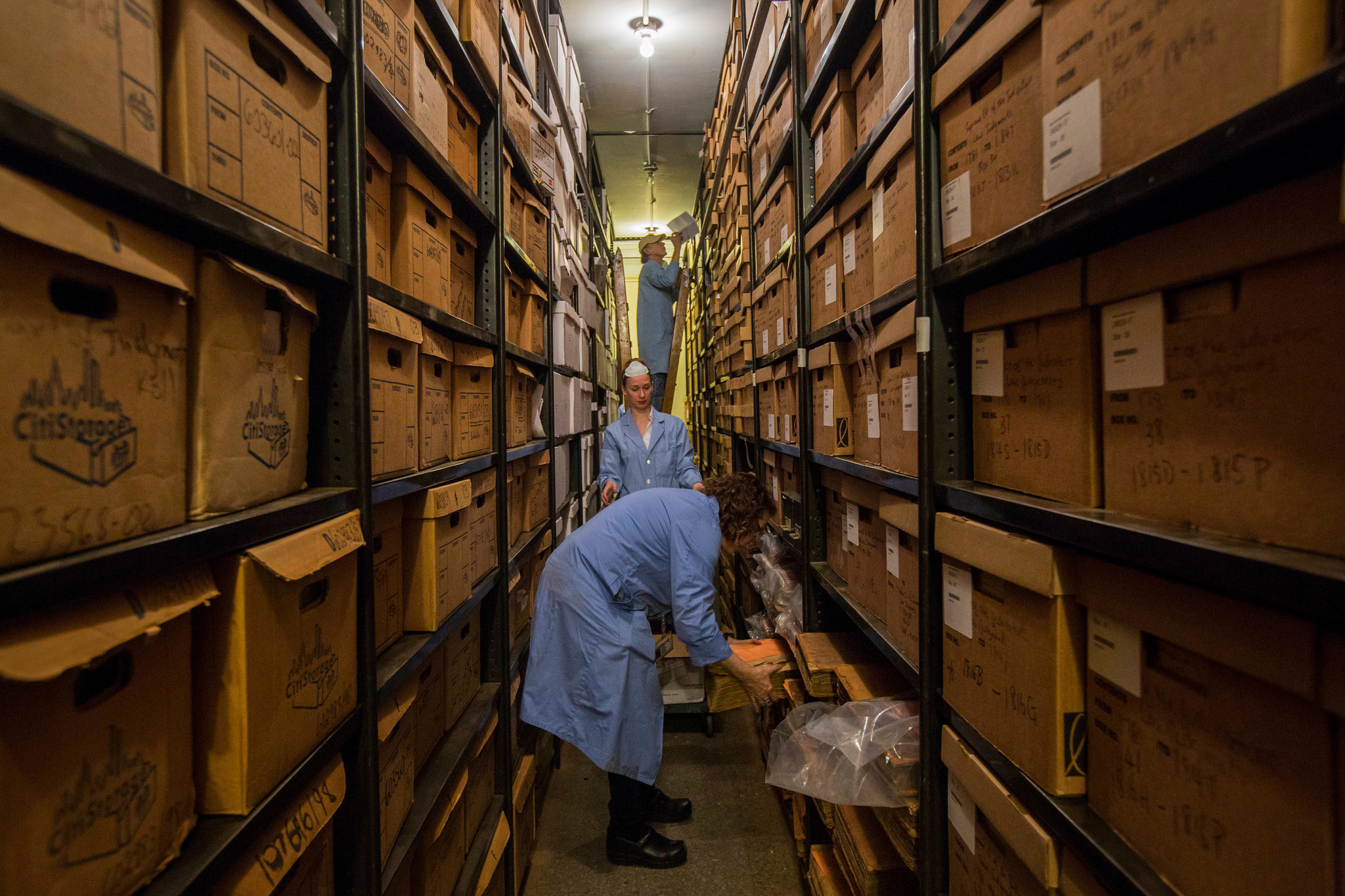 Color photo of archivists in lab coats moving old boxes.