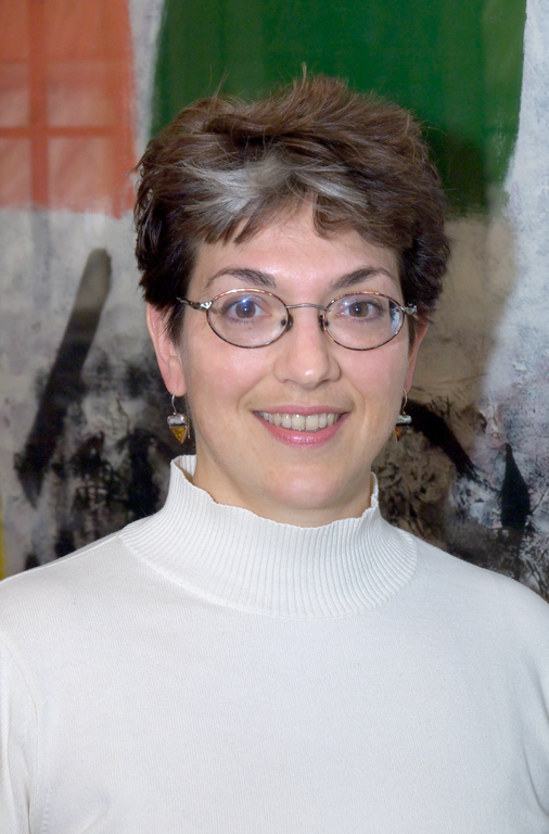 Marquis smiles at the camera. She is wearing a white turtleneck and heart-shaped earrings. 