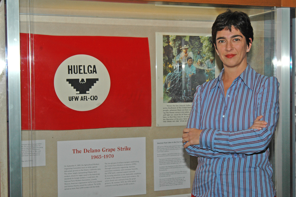 Mieri stands in front of an exhibit case with a panel, titled "The Delano Grape Strike." In the case