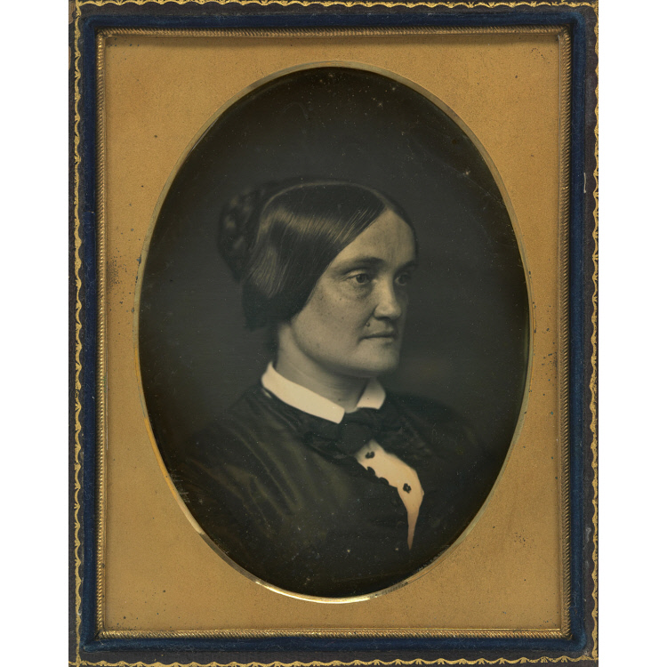 Black and white half-plate daguerreotype of a woman seen from the chest up, image is in a black frame
