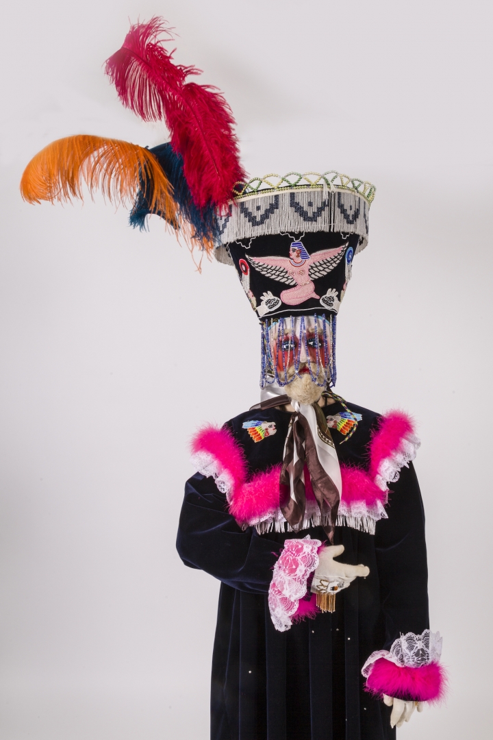 Fully dressed model in black robe with pink collar and sleeves and elaborate headdress with bright f