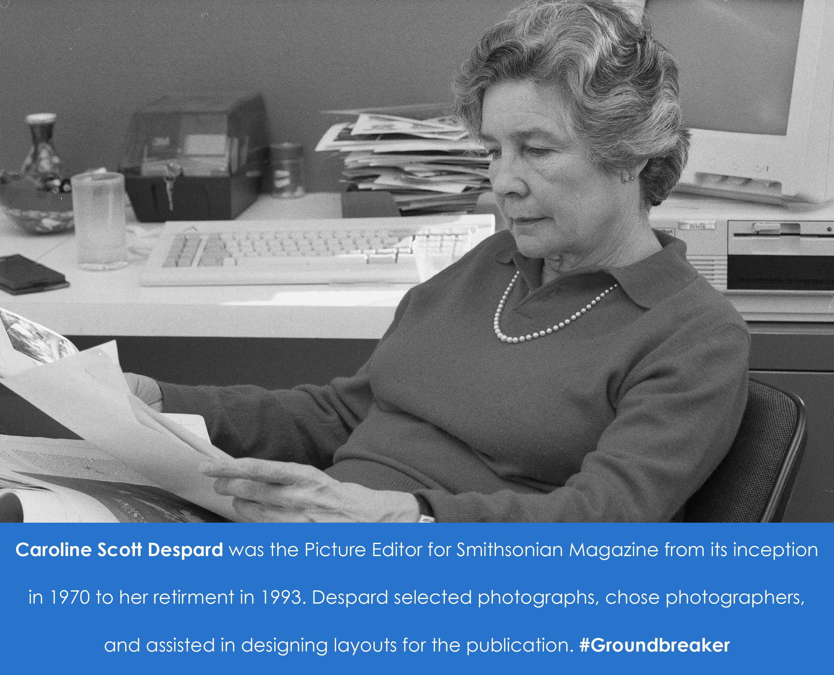 A woman sits at a desk, and appears to be reading a paper.