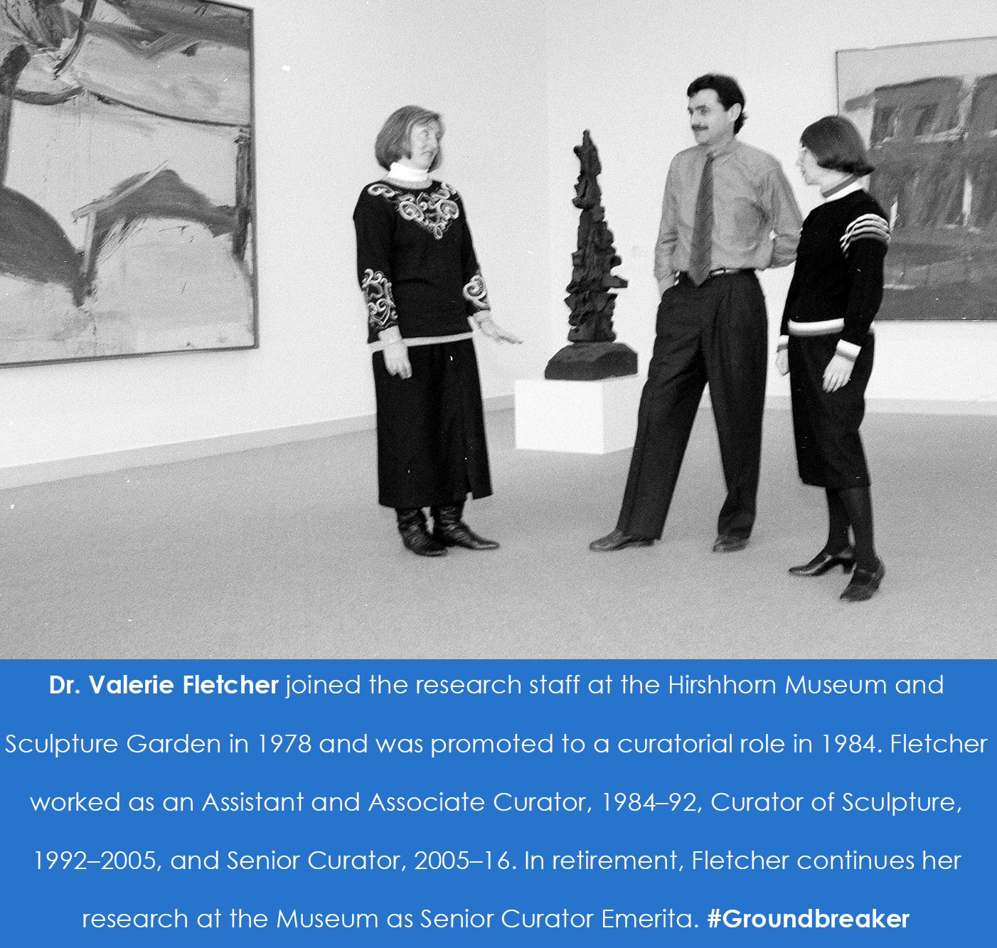 Valerie Fletcher stands and talks with two other people in a gallery space in front of a sculpture a