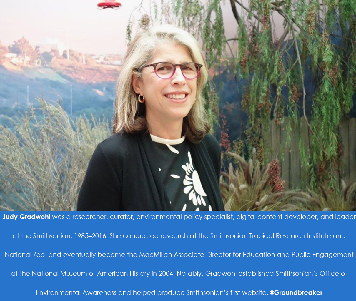 A woman wearing glasses poses for a photograph in front of nature scene. 