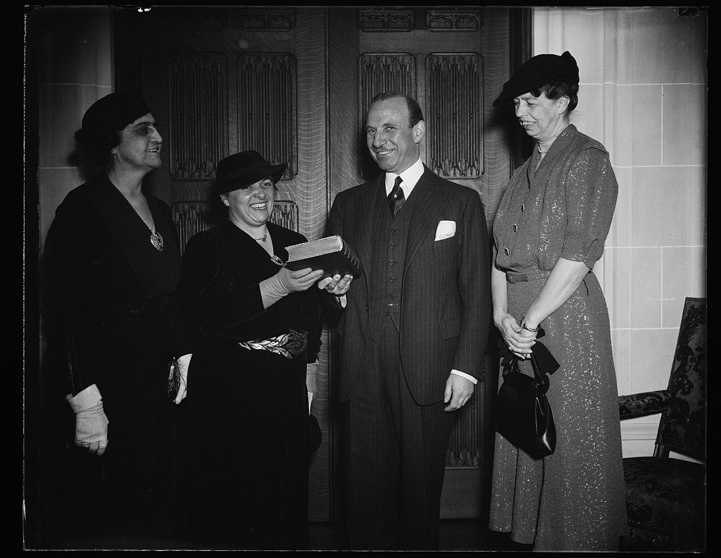 Black and white photo of Marjorie B. Illig, presenting a book to Jule Henry as Eleanor Roosevelt loo