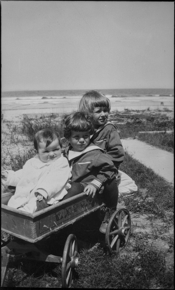 Joseph P. Kennedy, Jr., John F. Kennedy, Rosemary Kennedy as children sitting together in a wagon on the beach.