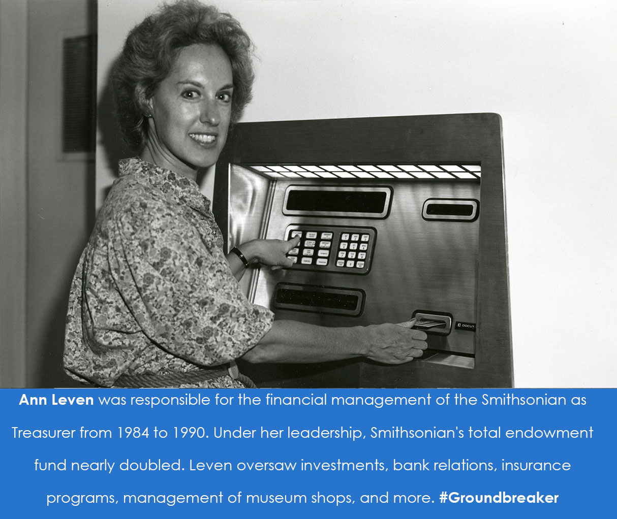 A woman holds a card up to a slot in an ATM machine. She turns to smile at the camera.