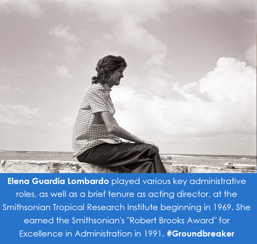 Black and white photograph of Lombardo sitting on rocks overlooking the ocean. 