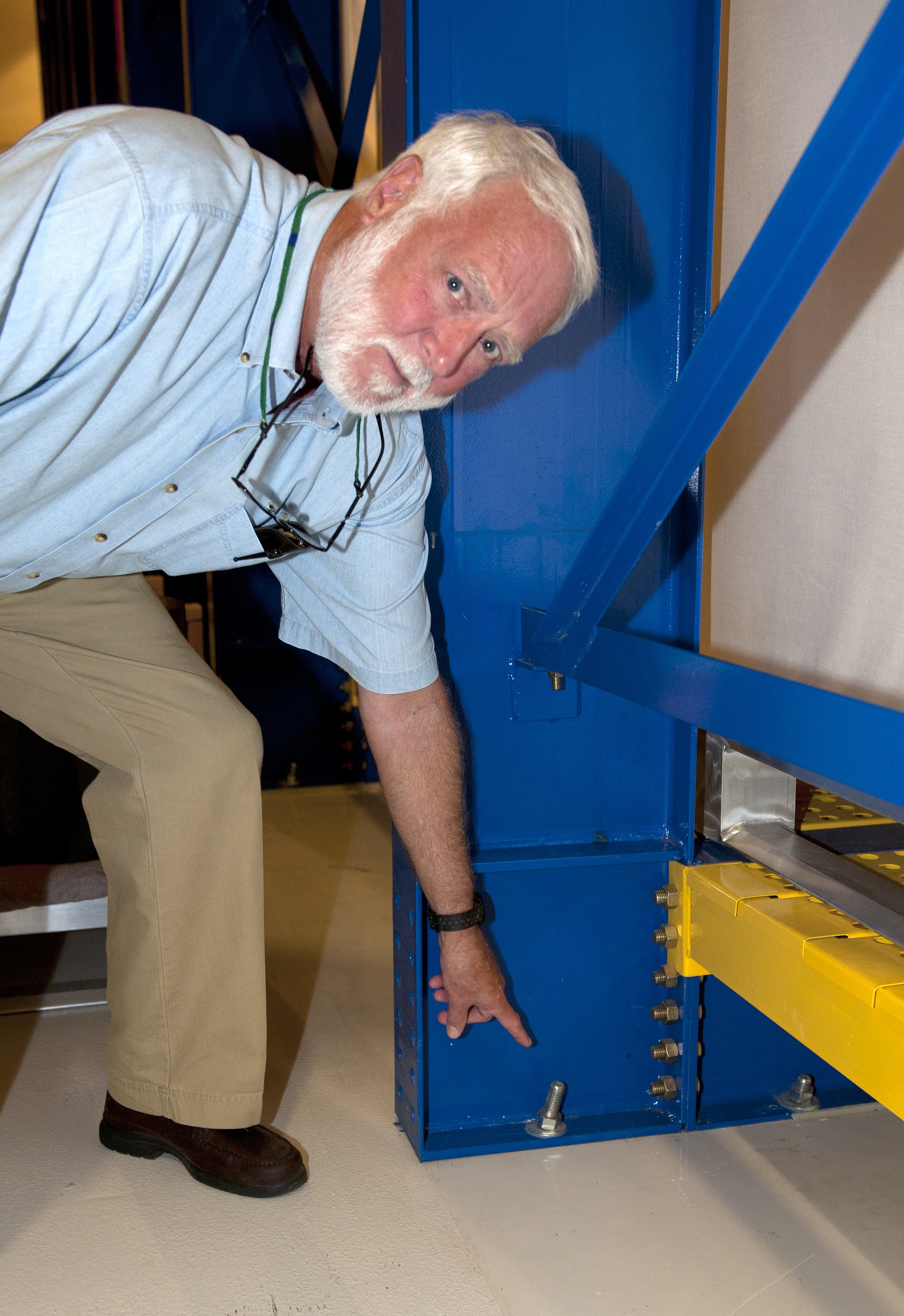 A man points to a bent bolt attached to a metal support.