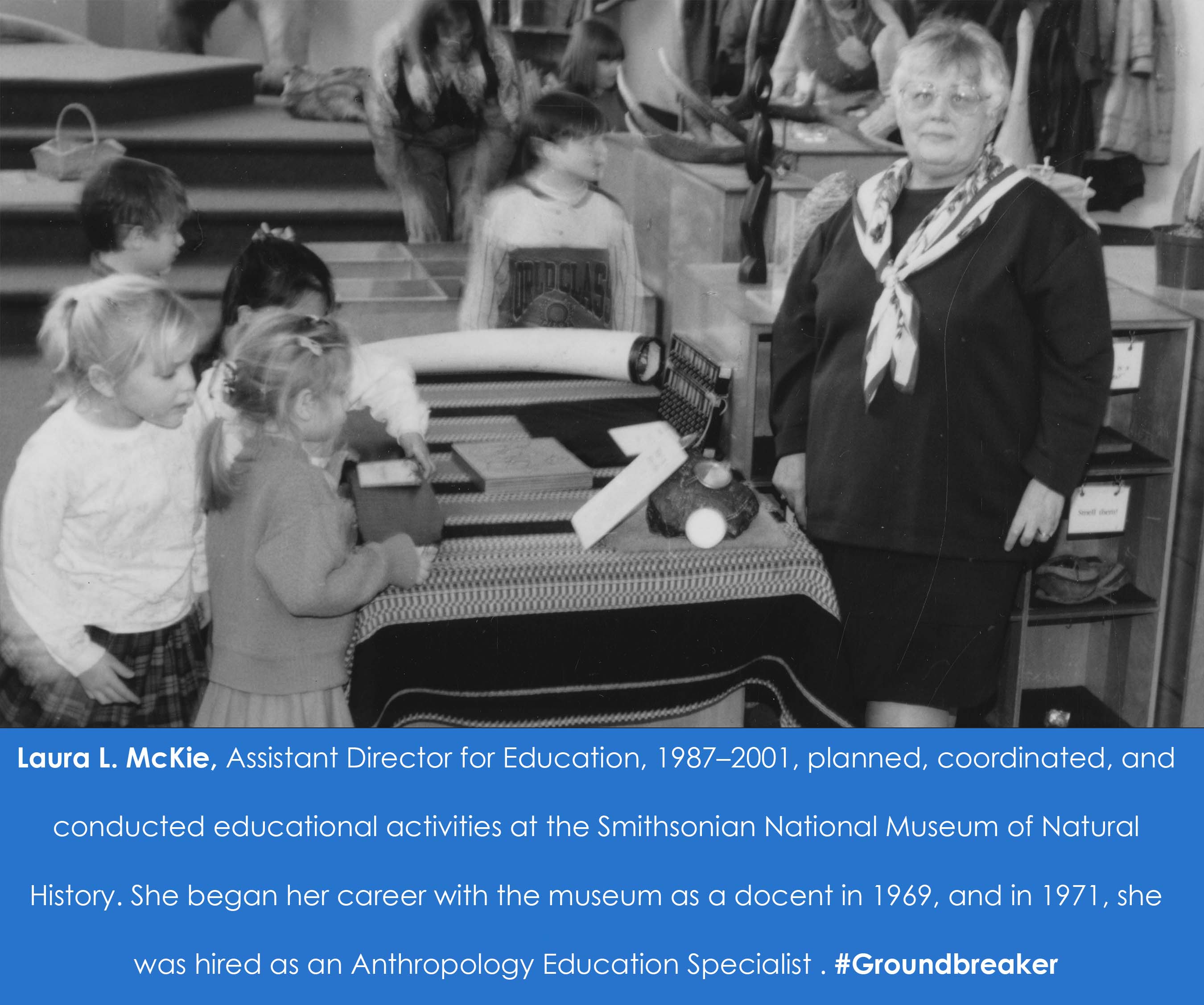 A woman stands near a table that children are working on. 