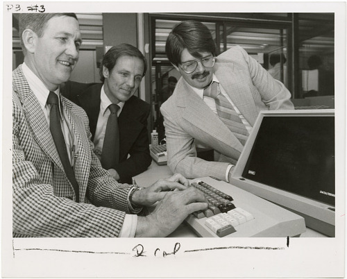 Three men test out new computer equipment. They are all wearing suits. 