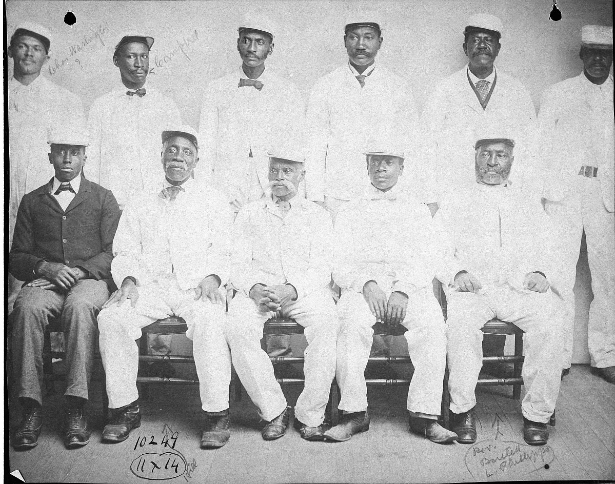 African American laborers pose for a photograph. All but one are wearing white uniforms. 