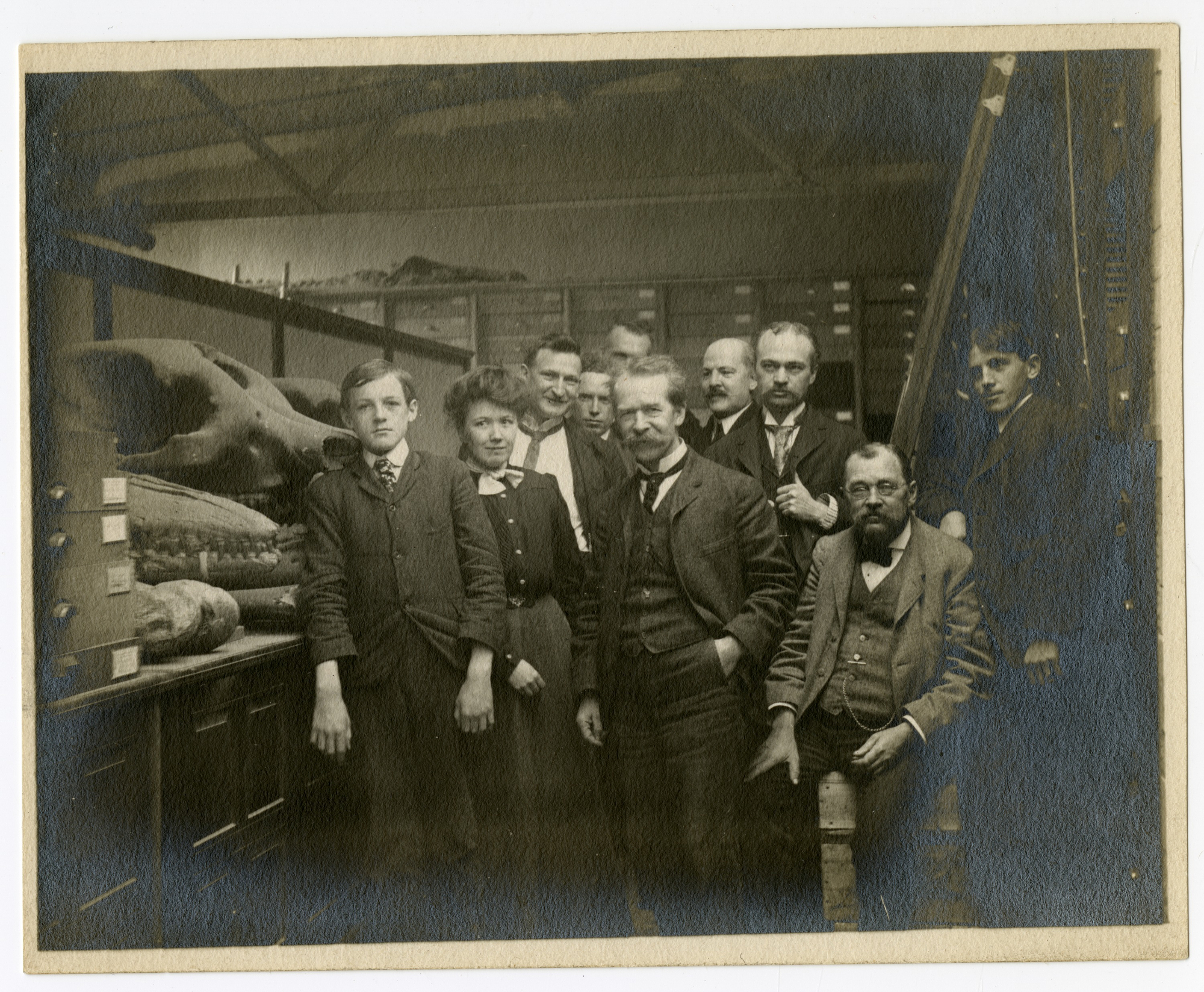 B&W group photo of men and women with bones on shelves