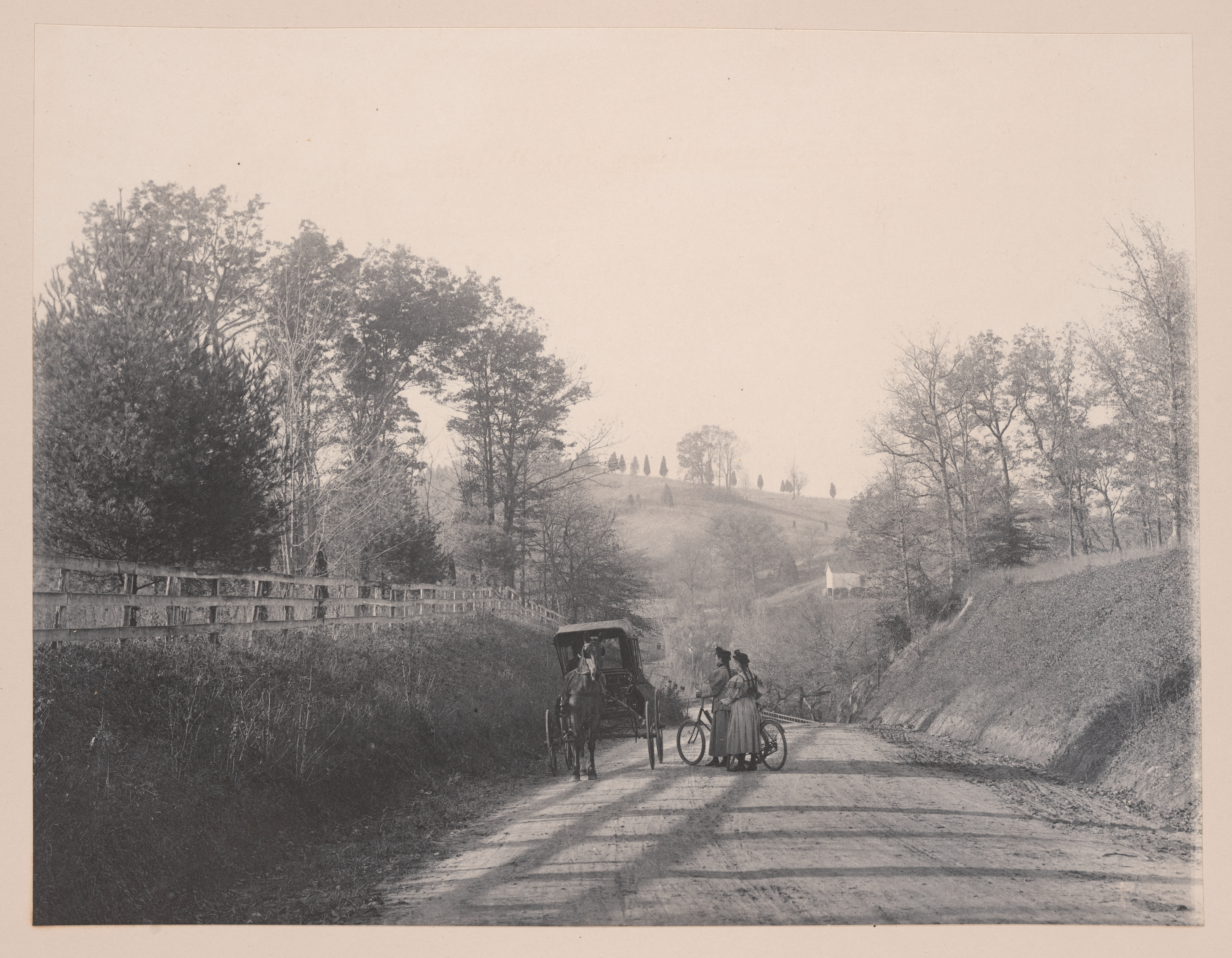 Two people sharing a bicycle stop near a horse and carriage on a dirt road. 