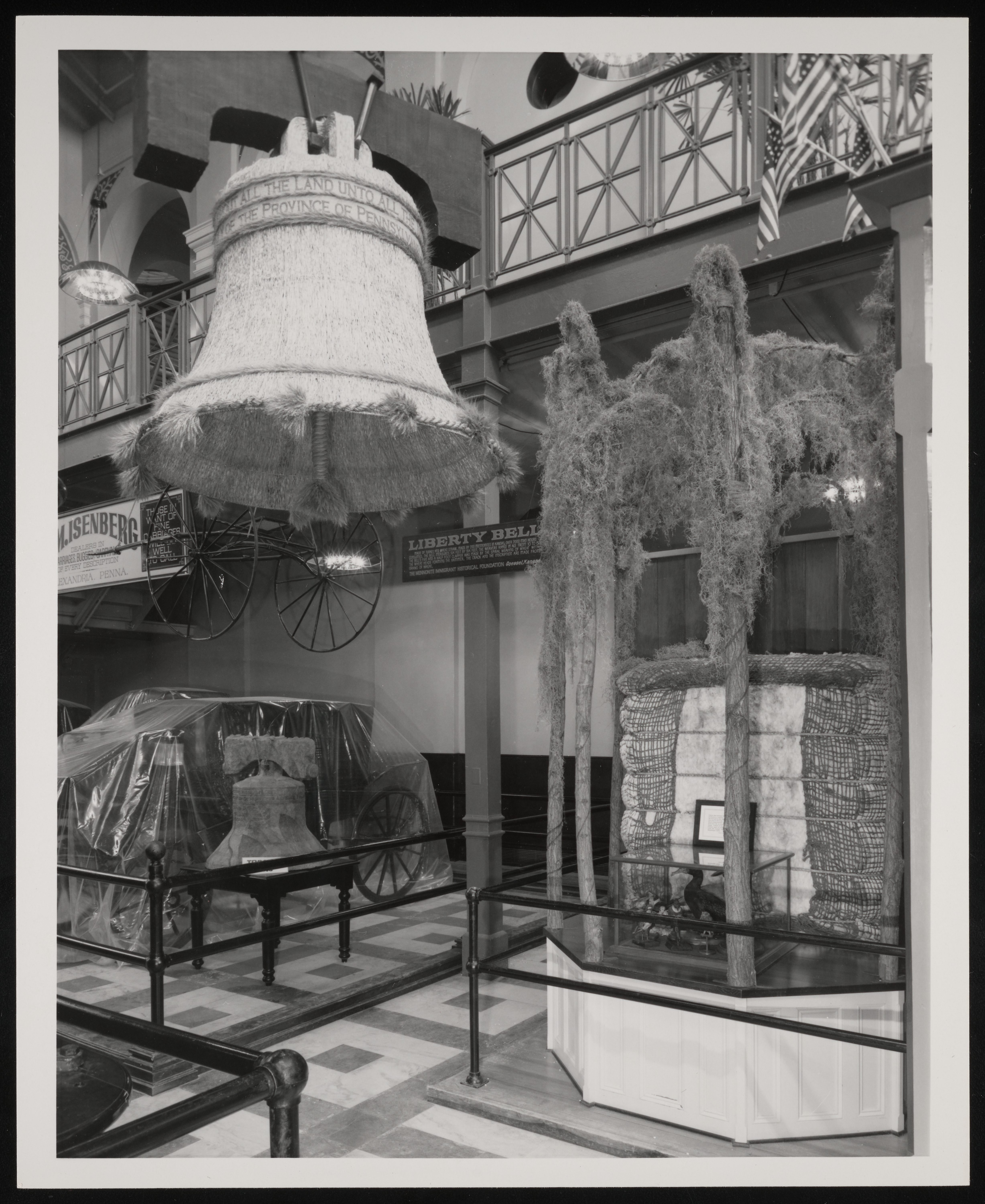  View of a corner of an exhibit that features a bell and a wagon. 