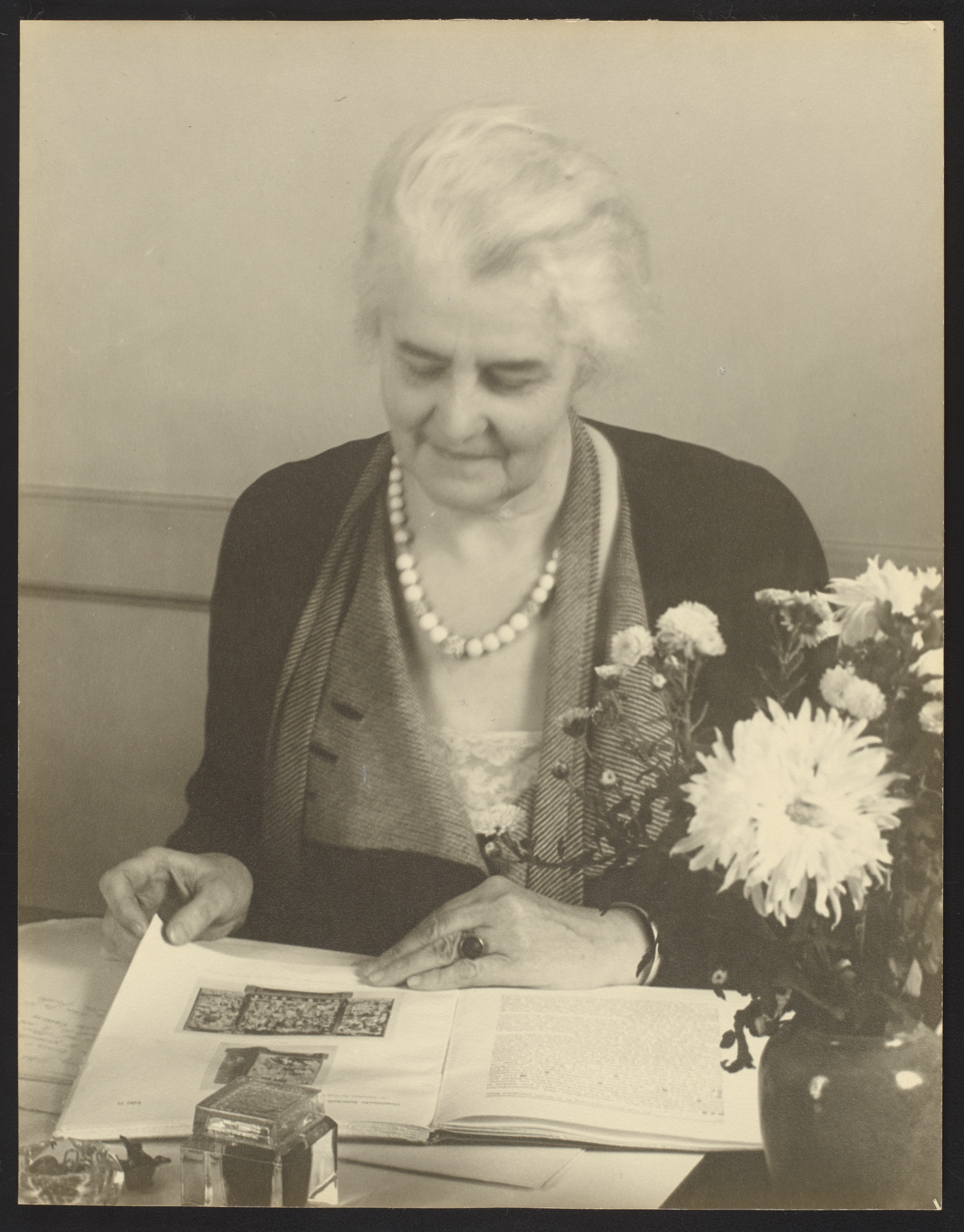 Portrait photograph of Guest seated at a desk. She has a book open and is looking down at it.