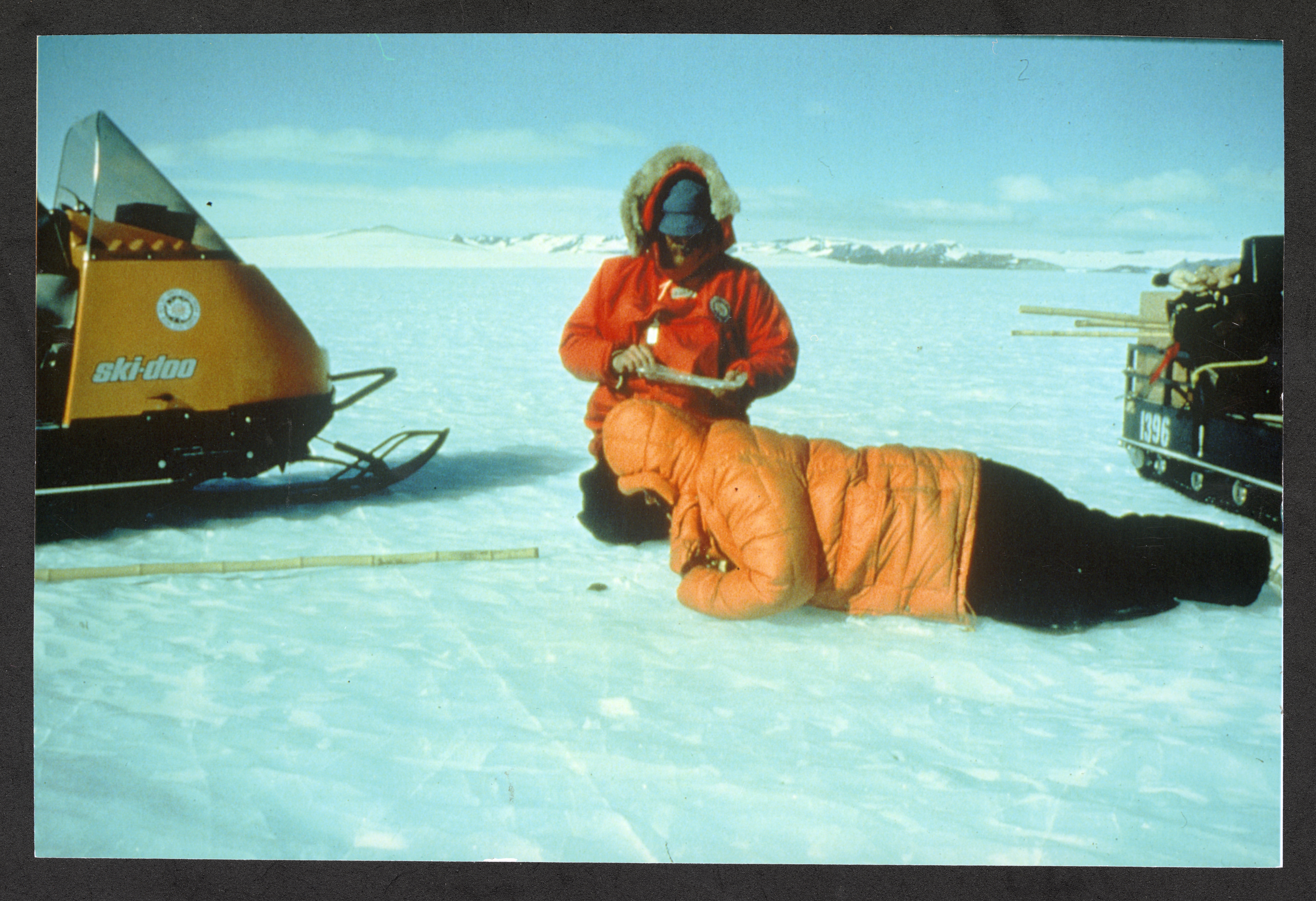 Ursula Marvin lies on her stomach to look into ice. A colleague kneels next to her, taking notes.