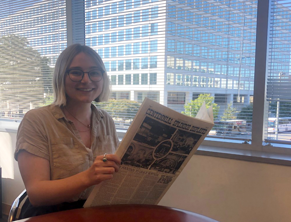 A person sits at a tables holding up a newspaper.