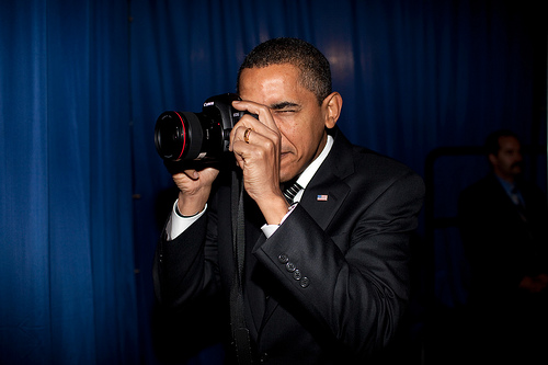 President Barack Obama takes aim with a photographer's camera backstage prior to remarks about provi
