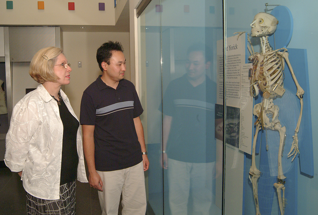 Interior view of two visitors looking at a skeleton with prosthetics behind glass.