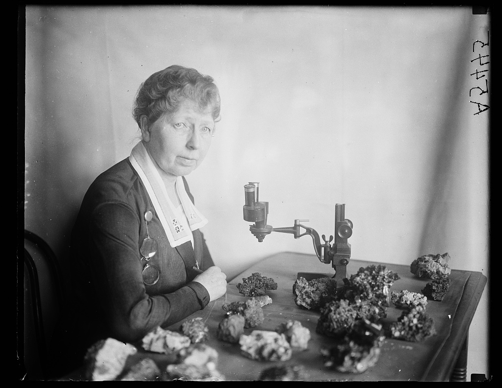 A woman sitting at a table looks at diamond-bearing rocks under a microscope. 