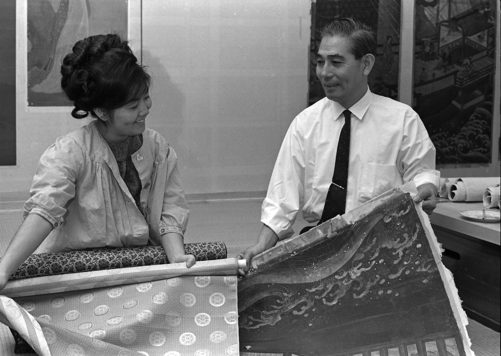 Takashi and Kumi Sugiura smile at one another as they hold up art and fabric.