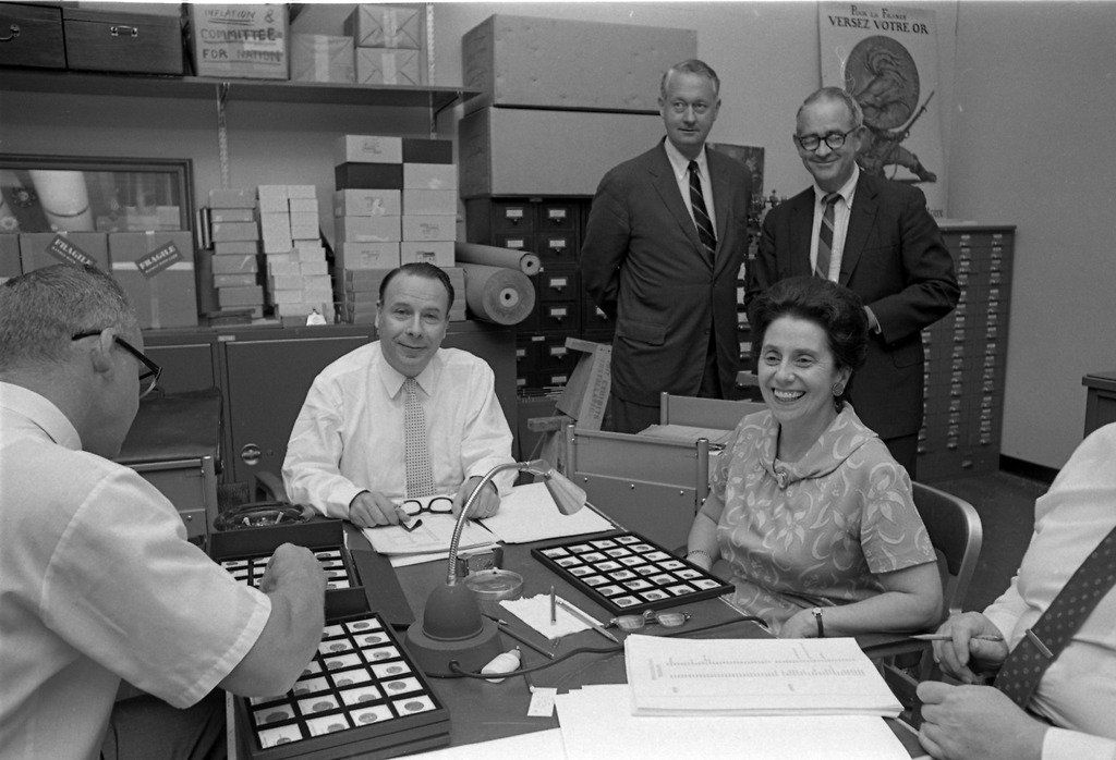 A man and woman stand in front of four exhibit cases of coins and paper currency. 