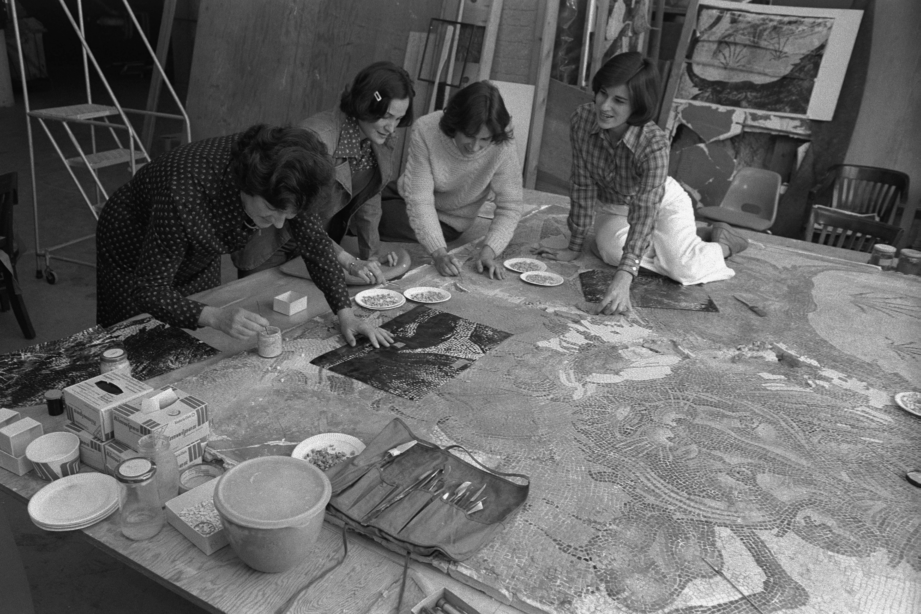 Four women work on a mosaic on some sort of base. 