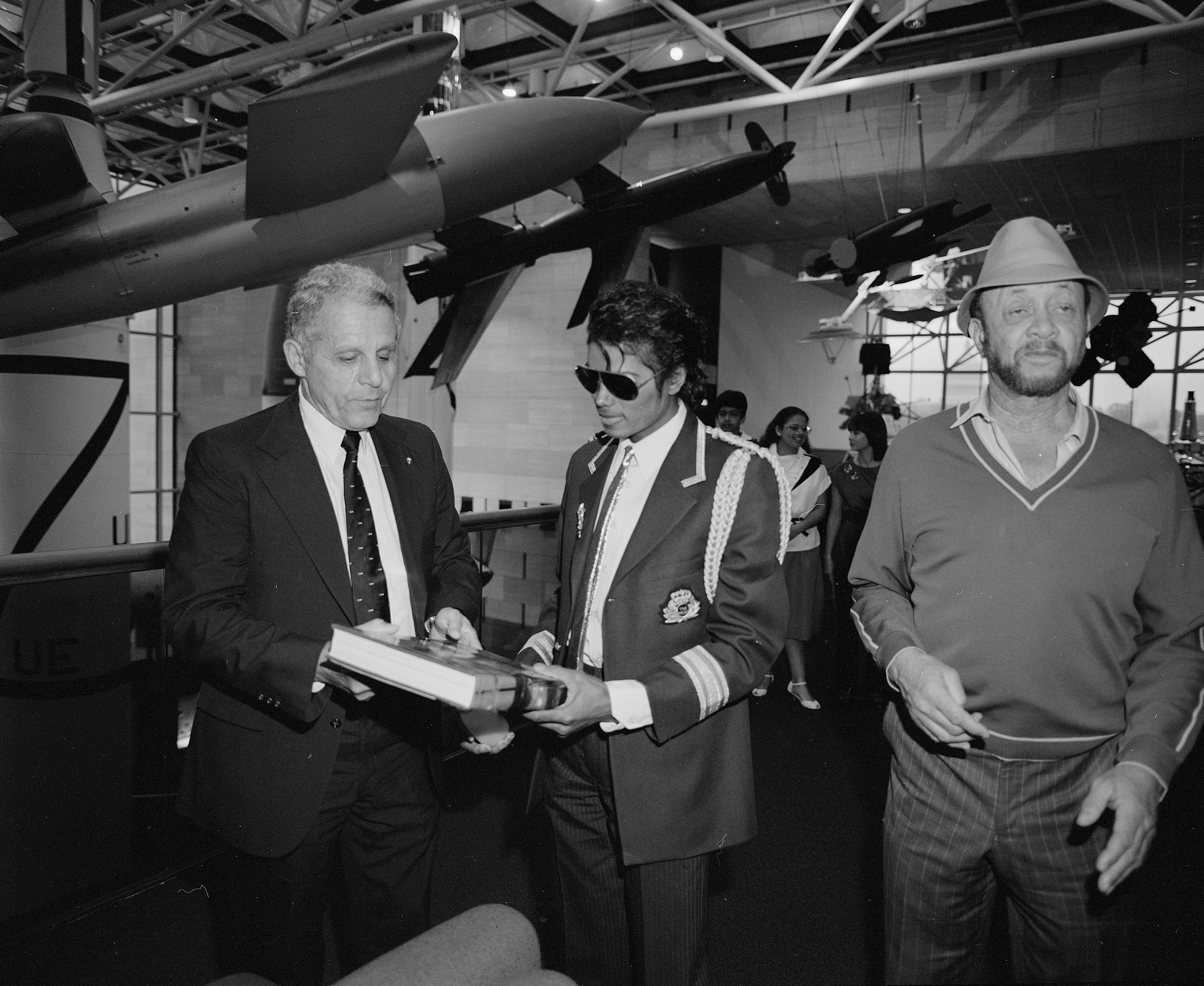 Two men stand in between Michael Jackson and the National Museum of Air and Space. Hanging airplanes are visible in the background. 