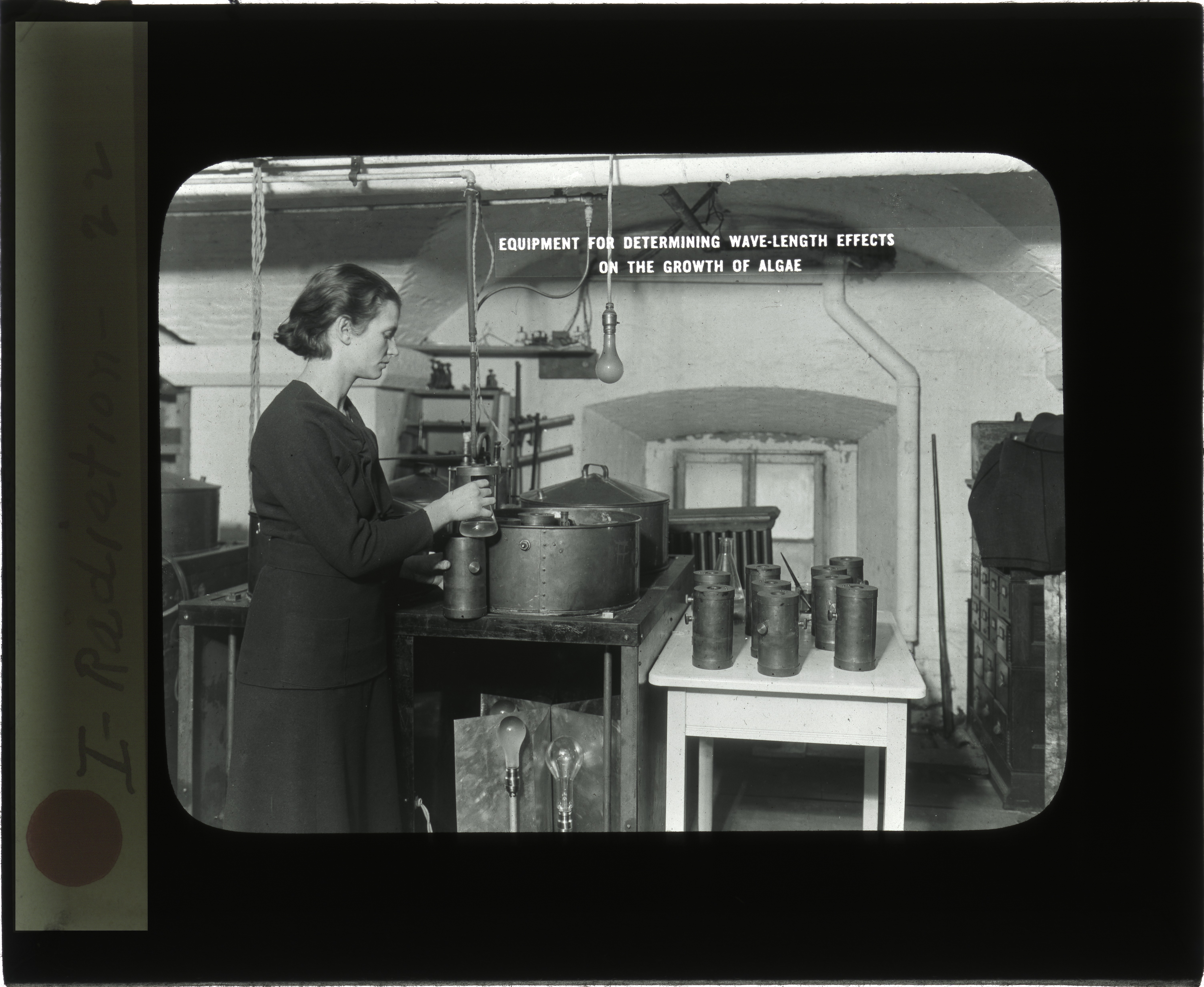 A person stands in a room with scientific instruments. She appears to be working on an experiment.