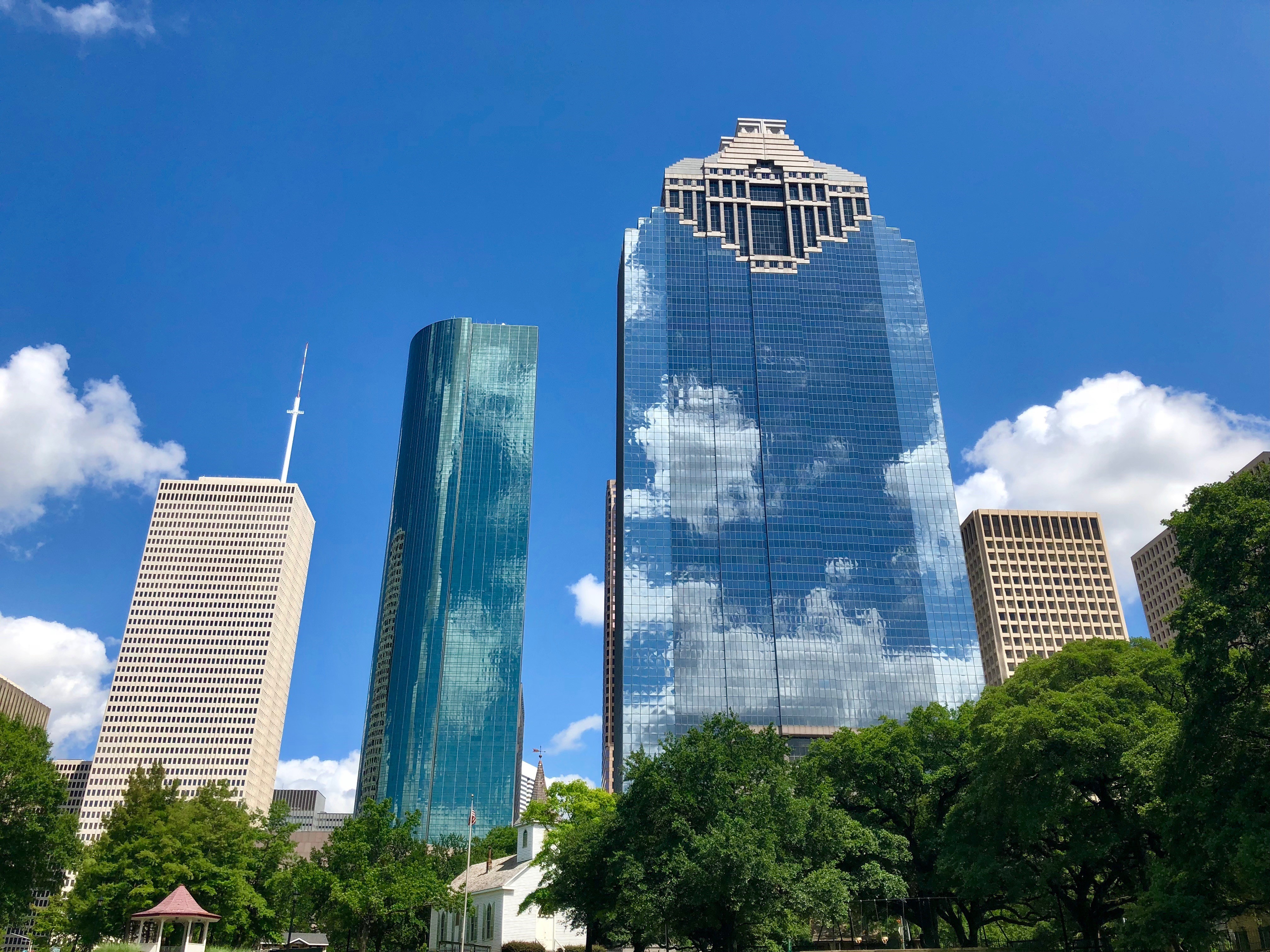 Color image of tall glass covered buildings, making up the Houston skyline, against and almost completely blue sky.