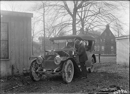Unidentified man polishes kerosene oil side carriage lantern on an automobile.