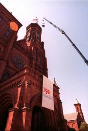 Images shows the a bell, made for the Smithsonian Institution's 150th anniversary, being hoisted to 