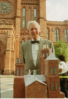 Secretary I. Michael Heyman is standing behind a birthday cake shaped like the Smithsonian Instituti