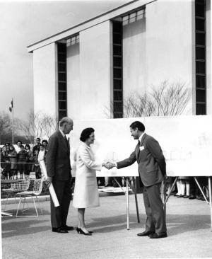 Man in suit shaking hands with a woman outside in front of the National Museum of American History b