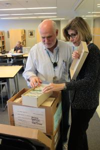 Two volunteers standing shoulder-to-shoulder over an archival box.