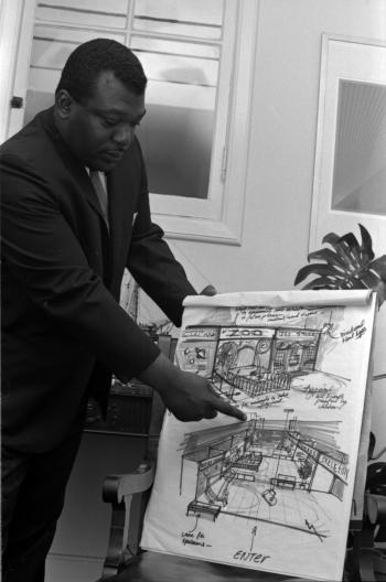 Black and white photograph of man pointing at concept drawing.