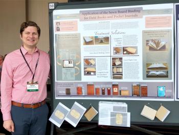 Color image of a man in a pink button down shirt standing next to a poster board presentation.