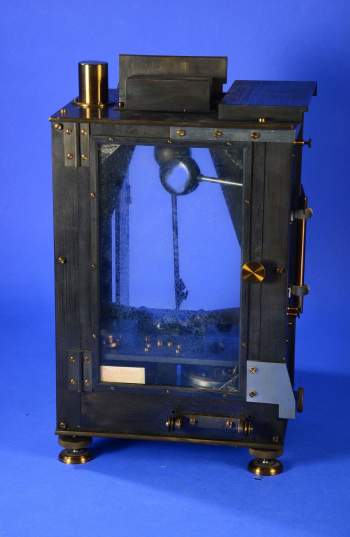 Color photo of a scientific instrument in front of a blue background, instrument is similar in appearance to a 19th century safe, with a clear front door.